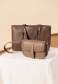 Kaksi nahkalaukkua: suuri, tummanruskea olkalaukku, jossa on kaksinkertaiset kahvat, ja pieni, vaaleanruskea olkalaukku, jossa on läppä ja solkikoriste.