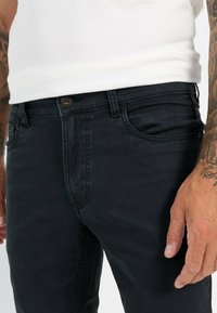 Black denim jeans with a soft texture, featuring a classic five-pocket design, a metal button closure, and visible stitching details.