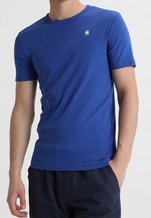 Sininen lyhythihainen t-paita, joka on valmistettu pehmeästä puuvillakankaasta. Siinä on pyöreä kaulus ja pieni logo vasemmassa rintataskussa. Rennon mallinen.