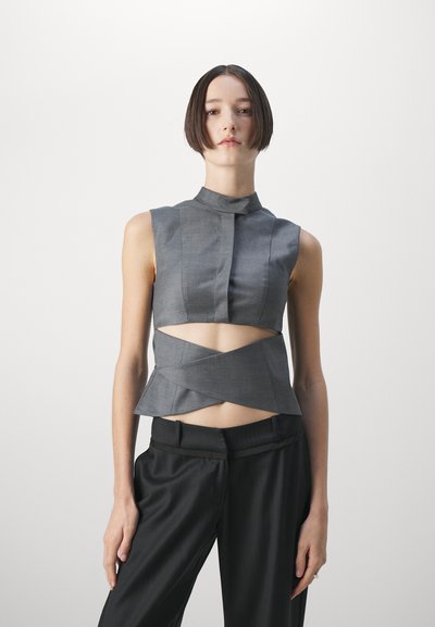 Gray sleeveless top with a high collar, cut-out design, and layered peplum hem, paired with black tailored trousers. Smooth texture.