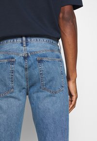 Jeans de mezclilla azul con un corte relajado, que cuentan con dos bolsillos traseros y un acabado desgastado. La tela tiene una textura suave y un diseño clásico.