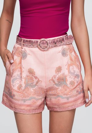 Femme portant un short taille haute rose à motifs avec ceinture et un top moulant sans manches magenta, les mains reposant près des poches.