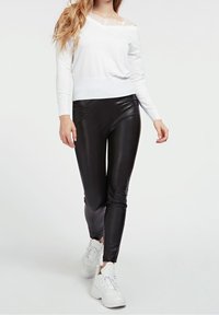 Maglietta bianca a maniche lunghe con dettagli in pizzo, abbinata a leggings neri lucidi e sneakers bianche. Tessuto liscio, design aderente e look moderno.