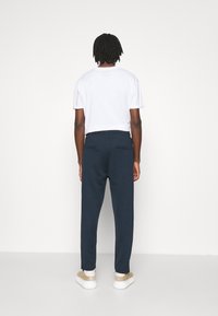 Marineblaue, schmal zulaufende Sweatpants mit Gesäßtaschen, kombiniert mit einem schlichten weißen T-Shirt und beigen Sneakers. Glatte Stofftextur, lässige Passform.