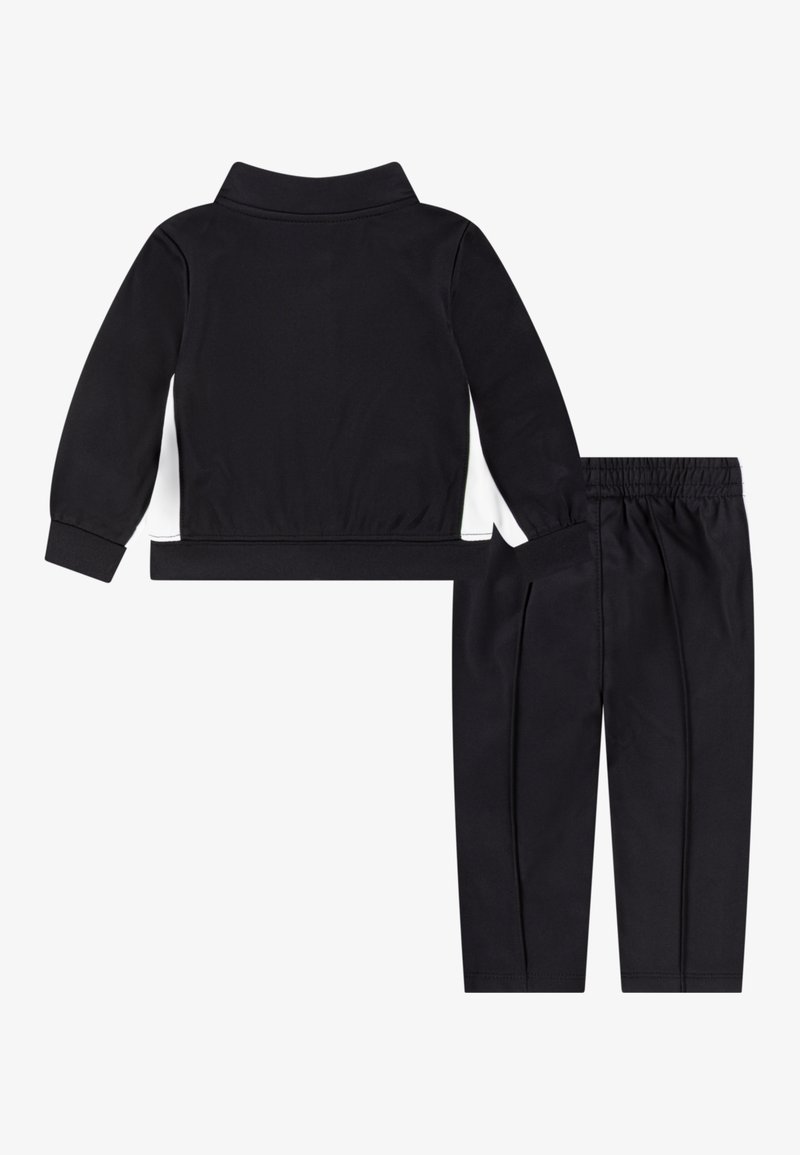 Tuta sportiva nera con giacca con zip e pannello laterale bianco, abbinata a pantaloni con vita elasticizzata e strisce laterali.