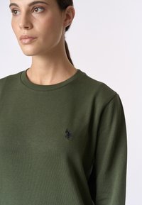 Felpa in cotone verde con scollo tondo, dotata di un piccolo logo ricamato blu navy sul petto e una texture liscia.