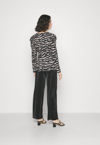 Haut à manches longues en motif zèbre noir et beige avec des détails froncés aux épaules, associé à un pantalon large plissé noir et des talons aiguilles noirs.