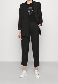 Svart dubbelknäppt kavaj med uppvikta ärmar, kombinerad med svarta byxor. Under kavajen en svart t-shirt med en glittrande karakt ärsdesign. Vita sneakers.