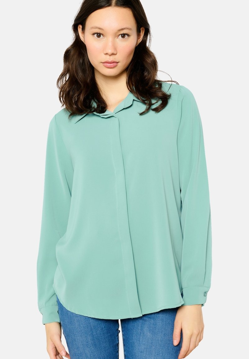 Light green long-sleeve blouse with a point collar, buttoned front, and a soft, smooth texture, paired with denim jeans.