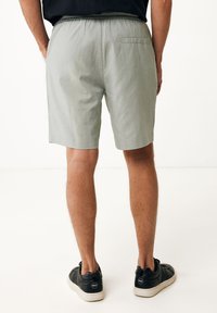 Ljusgrå shorts med resårmidja och bakficka, kombinerat med svarta sneakers. Tyget verkar lätt och slätt.