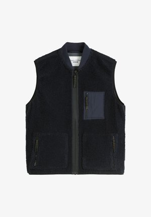 Mørkeblå fleece-vest med glidelås foran. Har en venstre brystlomme og to glidelåslommer på siden. Myk tekstur og sans for ermeløst design.