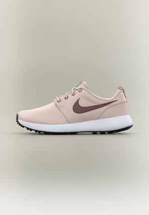 Baskets Nike rose clair avec un logo swoosh marron, une semelle blanche et une bande de roulement noire, vues de côté sur un fond neutre.