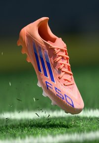 Scarpa da calcio arancione brillante con accenti blu, superficie testurizzata e design a tre strisce prominenti. Caratterizzata da una forma leggera e aerodinamica.