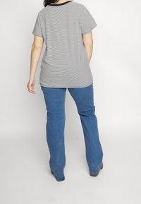 Pruhované černobílé tričko s krátkým rukávem, v kombinaci s modrými rozšířenými džíny. Tričko má černý lem u krku a pohodlný střih.