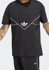 Svart Adidas-t-shirt med vit kant som formar en chevronform och Adidas trefoil-logga centrerad på bröstet.