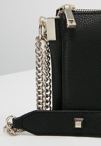 Czarna skórzana torebka z teksturowanym wykończeniem, srebrnymi akcentami, łańcuszkowym paskiem oraz metalowym akcentem na spodzie.