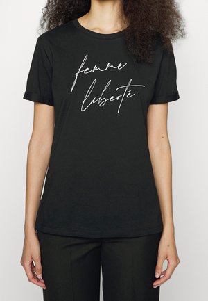 Kobieta ubrana w czarny t-shirt z podwiniętymi rękawami, na którym z przodu białym kursywą jest napisane "femme liberté".