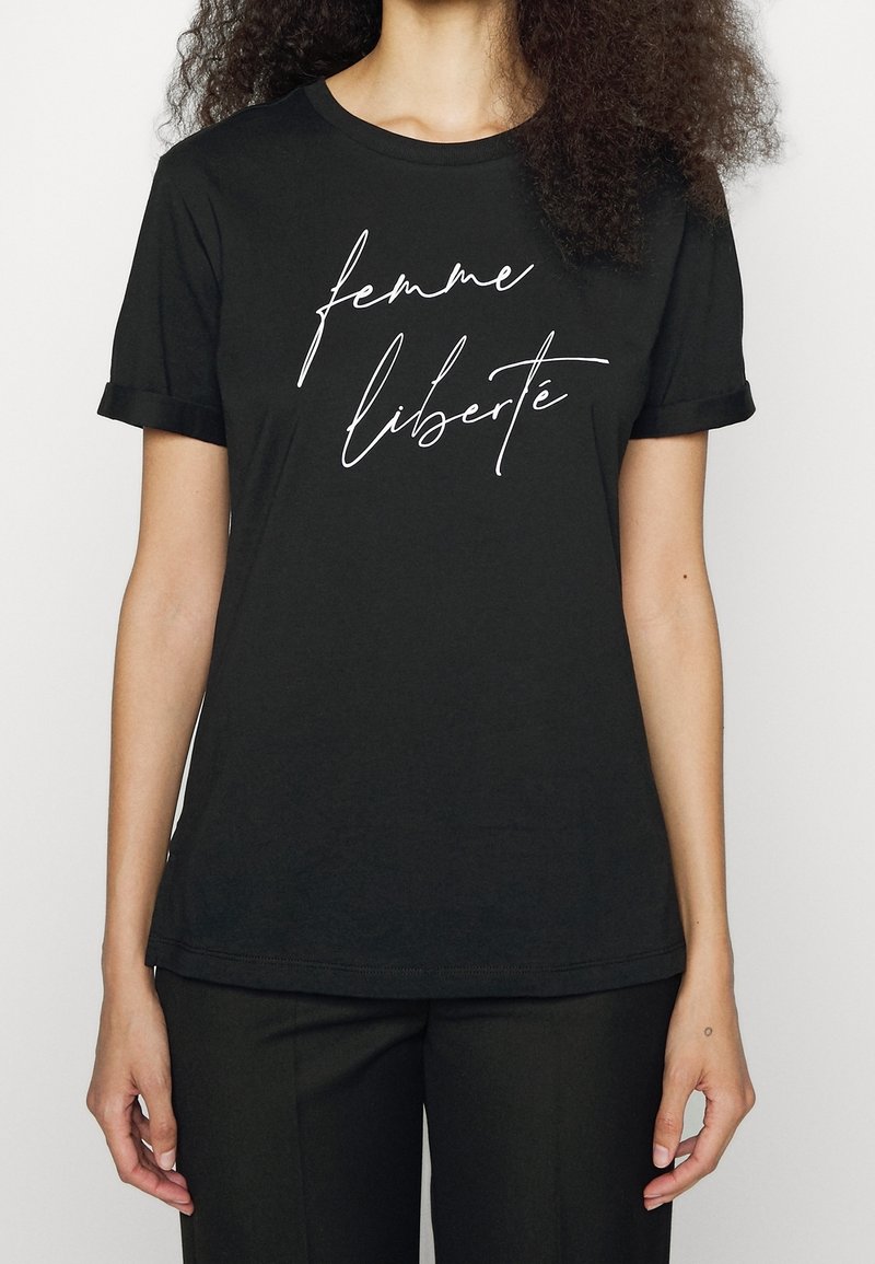 Femme portant un t-shirt noir à manches retroussées sur lequel est écrit en cursive blanche sur le devant "femme liberté".