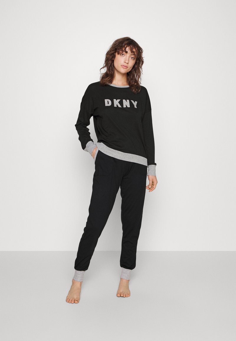 Sudadera negra con letras "DKNY" en plata, puños grises. Pantalones negros con puños grises. El material parece suave; ajuste relajado.
