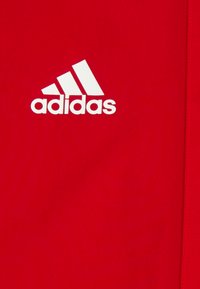Tessuto atletico rosso con un prominente logo Adidas bianco e tre strisce, texture liscia e cuciture pulite lungo i bordi.