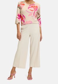 Beige floral sweater with pink and red patterns, paired with light beige wide-leg trousers and pink heeled sandals.