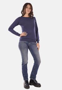 Maglione a girocollo navy in un tessuto morbido, abbinato a jeans blu e stivali neri chunky. Presenta un piccolo dettaglio del logo all'orlo.