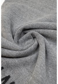 Tessuto grigio con un knit morbido e testurizzato, che presenta un motivo sottile. Il materiale appare leggero e si drappeggia senza sforzo in una spirale.