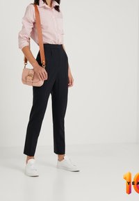 Světle růžová pruhovaná košile zasunutá do vysokých tmavě modrých kalhot, doplněná bílými teniskami. Malá růžová kabelka přes rameno se zlatým zavíráním.