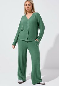 Ensemble de détente tricoté vert composé d'un cardigan à manches longues et col en V avec fermeture à boutons, ainsi que d'un pantalon à jambes larges. Texture douce, coupe décontractée.