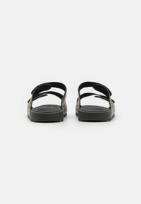 Des sandales noires à glissière avec des bretelles texturées et une semelle en caoutchouc plate, présentant deux boucles latérales ajustables pour un maintien sûr.