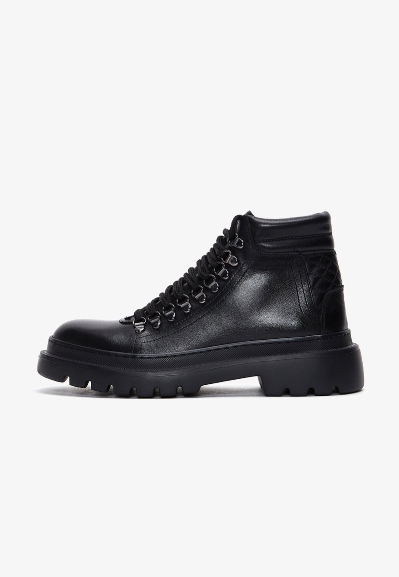 Bottine en cuir noir avec semelle épaisse à crampons, œillets crochet, col matelassé et détail matelassé au talon.