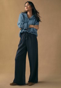 Pulover tricotat albastru deschis cu guler, asortat cu pantaloni negri largi și mocasini maro. Design simplu cu material texturat.