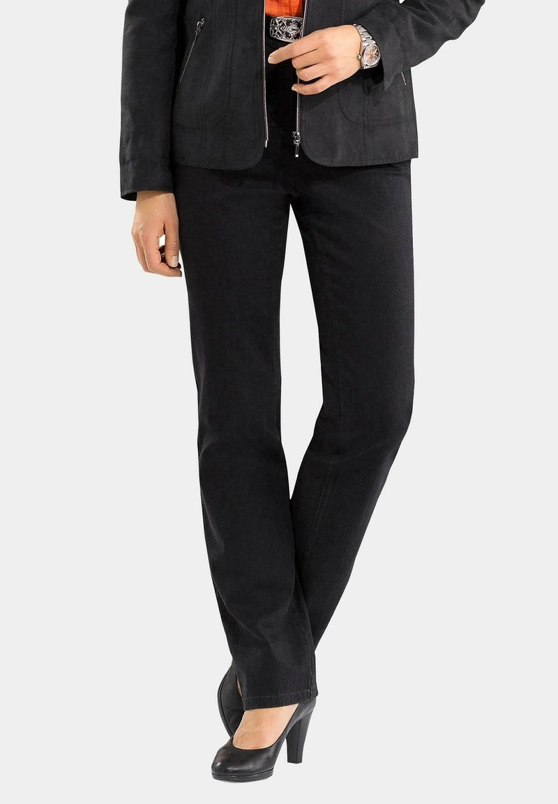 Schwarze gerade Jeans mit einer schwarzen Jacke mit Reißverschluss, kombiniert mit schwarzen High Heels. Das Outfit ist aus einem strukturierten Stoff gefertigt und zeichnet sich durch ein schlichtes Design aus.