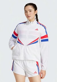 Weiße Sportjacke mit roten und blauen diagonalen Streifen, mit Reißverschluss und passender Shorts. Hergestellt aus leichtem, glattem Stoff.