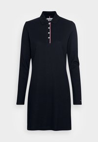 Svart långärmad polo-klänning med krage, fyra vita knappar och röd-vit-blå kant längs knappslået.