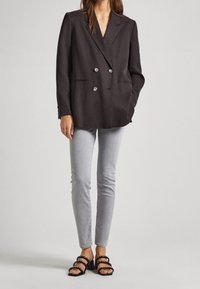 Blazer doble de botonadura en gris oscuro, de tejido texturizado, con botones grandes, combinado con jeans skinny gris claro y sandalias negras de tiras superpuestas.