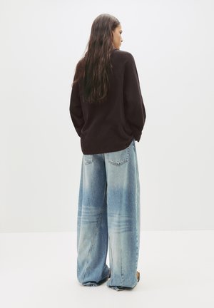 Maglione nero oversize con collo a giro, abbinato a jeans in denim azzurro chiaro larghi con motivi sbiaditi e una vestibilità rilassata.