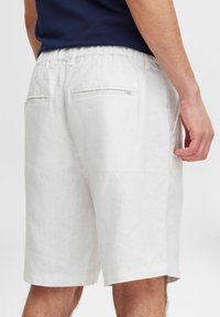 Hvite linsjeshorts har en avslappet passform med elastisk midje. To baklommer med minimale detaljer og en myk tekstur.