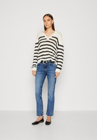 Stripet strikkegenser med v-hals i krem og svart, kombinert med blå denimjeans og svarte leiligheter. Enkelt design med en avslappet passform.