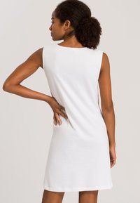 Vestido blanco sin mangas con un corte relajado, hecho de una tela suave. Presenta un escote redondo y cae por encima de la rodilla, mostrando un diseño limpio.