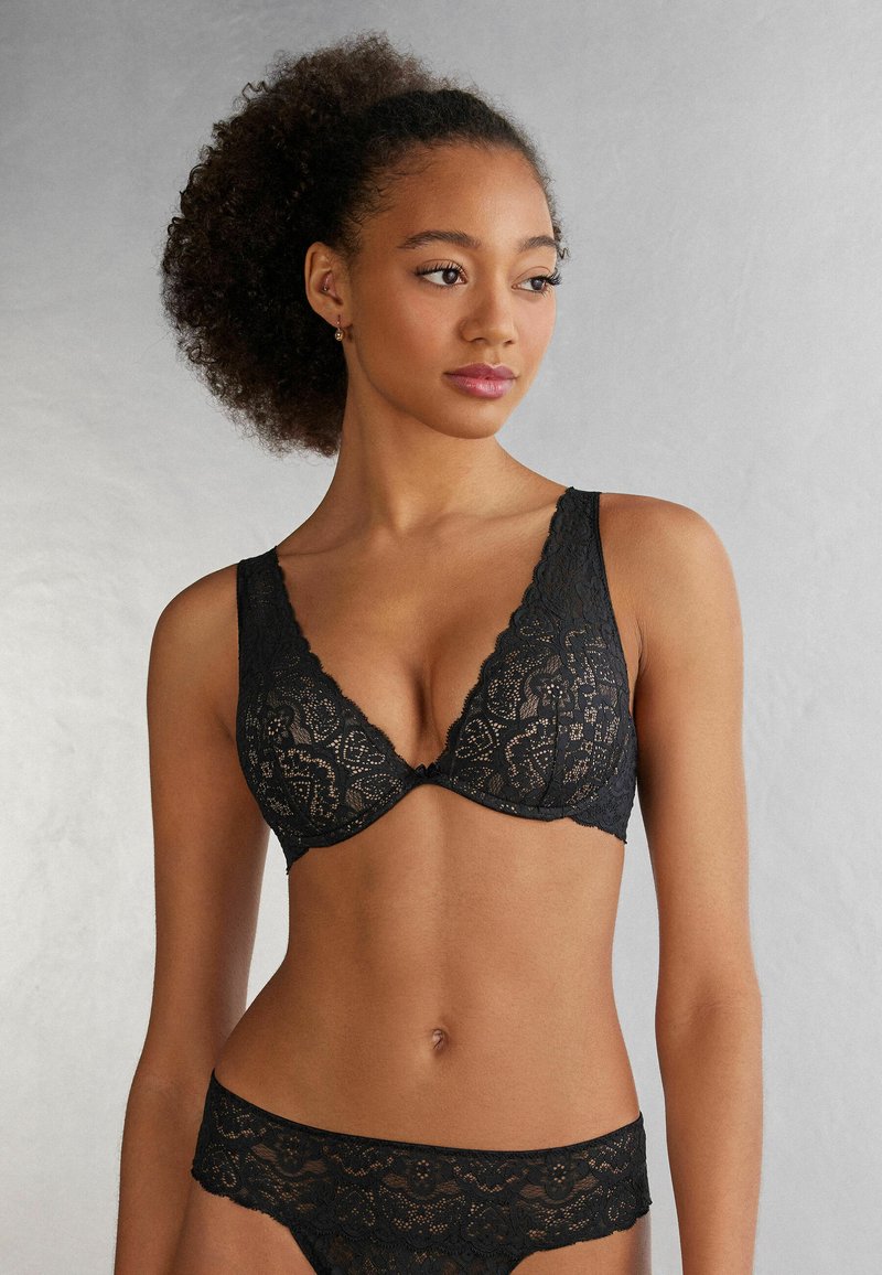Svart spets-BH med djup urringning och scalloperade kanter, tillsammans med matchande spetsunderkläder med blommönster.