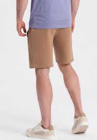 Un short en coton marron avec des poches latérales, une coupe décontractée et une texture lisse, associé à des baskets basses beiges.