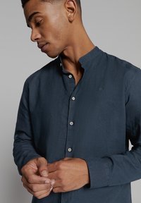 Marineblauwe button-up shirt met een bandkraag, gemaakt van textuurstof, met een subtiel logo en zichtbare knopen aan de voorkant.
