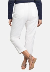 Witte katoenen broek met een relaxed fit, voorzien van twee achterzakken en opgerolde manchetten, gecombineerd met tan kleurige sandalen met bandjes, versierd met embellishments.