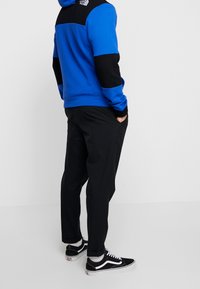 Modrá a černá barevně blokovaná mikina s černým logem, spárovaná s černými kalhotami a černými teniskami. Měkká textura a volný design.