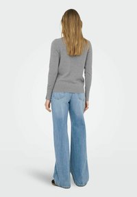 Grijze gebreide trui met lange mouwen en een rond decolleté, gecombineerd met lichtblauwe klokjeans. Zichtbare details op de achterkant en stiknaden.