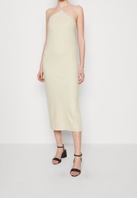Šaty s halter krkem, délka ke kolenům, v světle béžové barvě s vertikálním žebrovaným vzorem a jemným leskem. Doplněno černými blokovými podpatky s kotníkovým páskem.