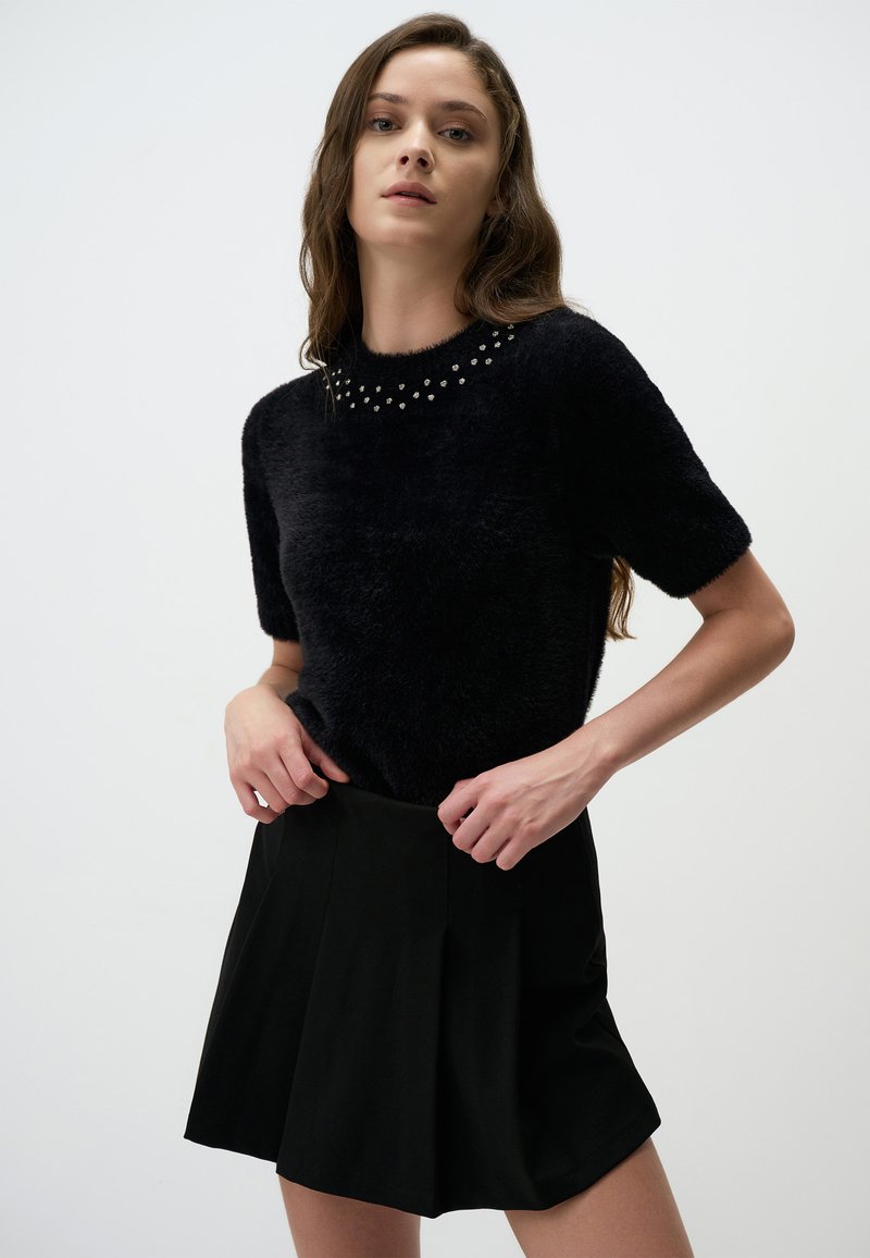 Czarny, puszysty, krótkorękawowy sweter wełniany z dekoracyjnymi ćwiekami przy dekolcie, zestawiony z czarną spódnicą plisowaną. Gładka faktura na całej powierzchni.