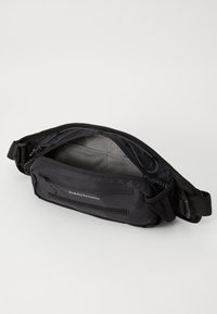 Black Peak Performance waist bag with multiple zippered compartments, adjustable strap, and mesh inner pocket, shown open on white background.