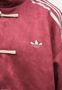 Μπουφάν Adidas σε μπορντό με λευκό λογότυπο trefoil στο στήθος και εκρού κορδόνια κοντά στον γιακά, που δείχνει λεπτομέρεια του άνω κορμού.